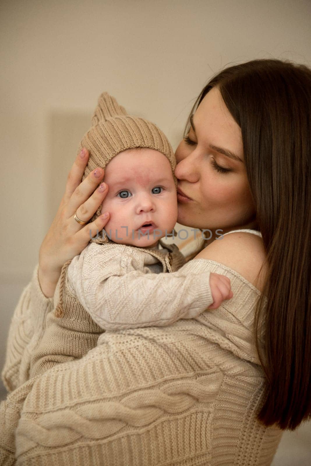 A woman holding a baby. High quality photo, The girl holds her child in her arms. The child is wearing a beige hand-knitted hat. mother and child are happy, they are smiling