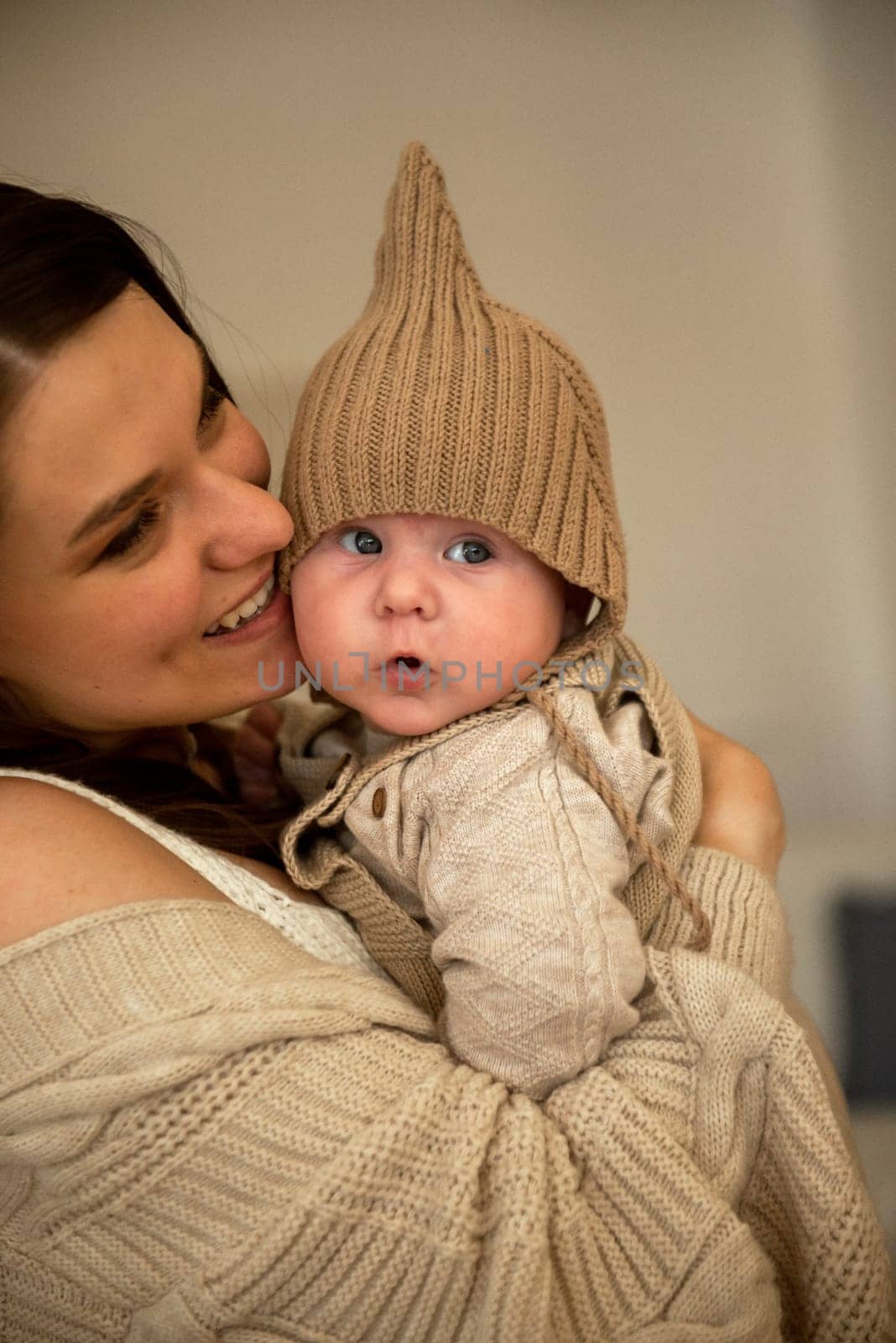 A woman holding a baby. High quality photo, The girl holds her child in her arms. The child is wearing a beige hand-knitted hat. mother and child are happy, they are smiling