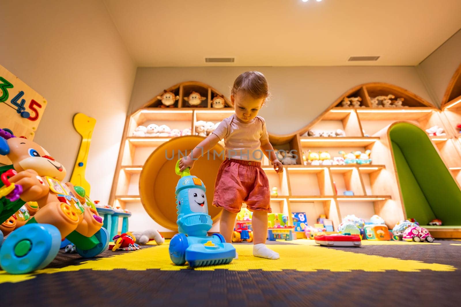 Toddler playing with a toy vacuum cleaner in a colorful and organized playroom for fun and learning