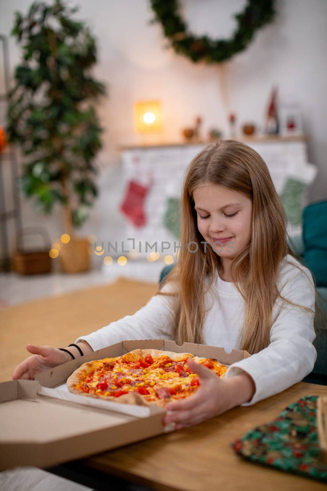 A cheerful and joyful child eagerly opens a pizza box in a warm, festive setting filled with vibrant holiday decor
