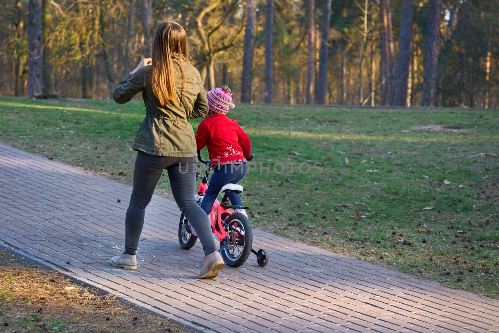 show or explain to someone how to do something. Cheerful mom teaches her child to ride a bike in autumn spring park.