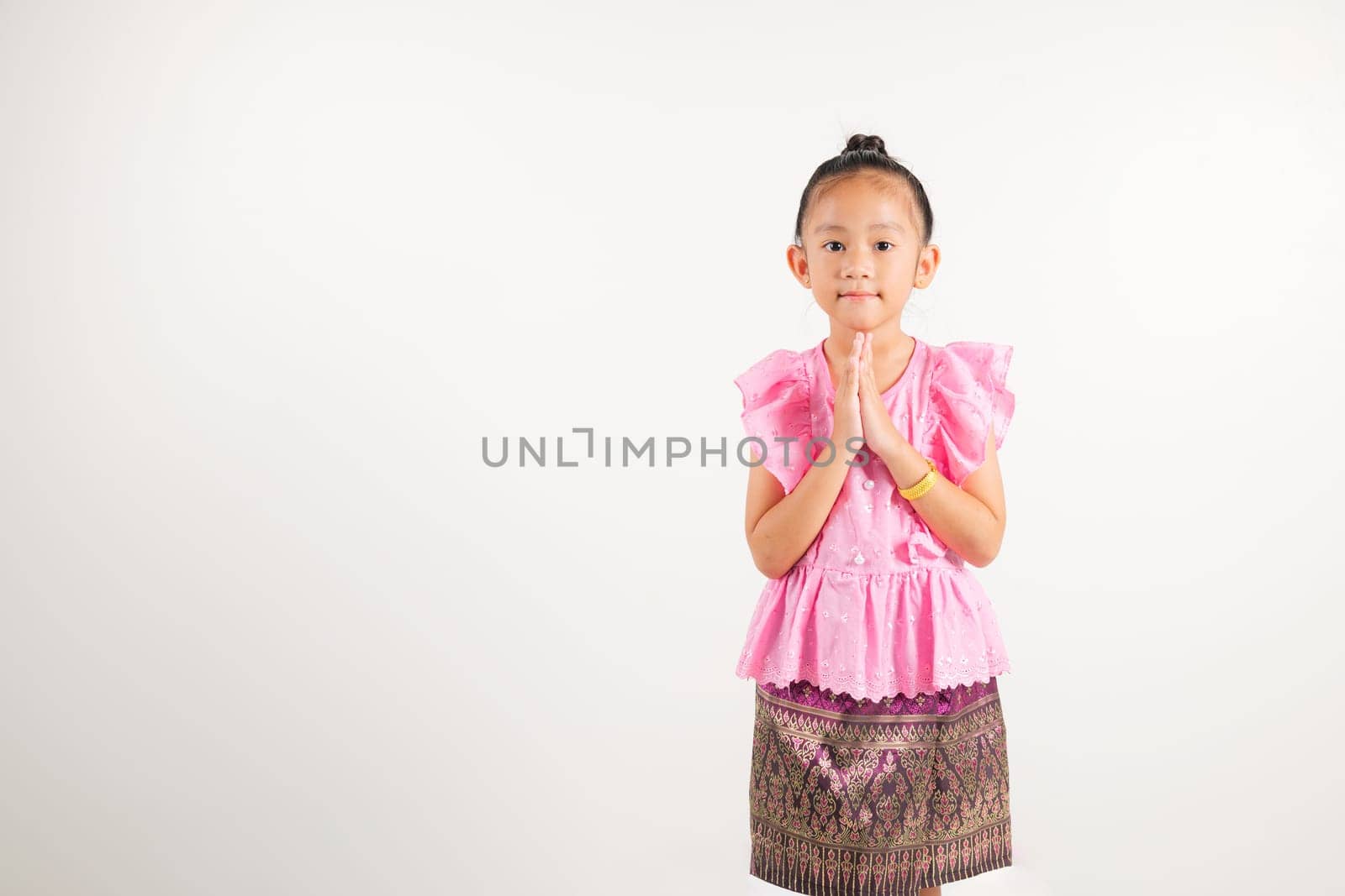 Portrait of Thailand kid girl smiling traditional Thai dress costume posing to pay respect in studio shot isolated white background, Happy kindergarten child sawasdee symbol or welcome