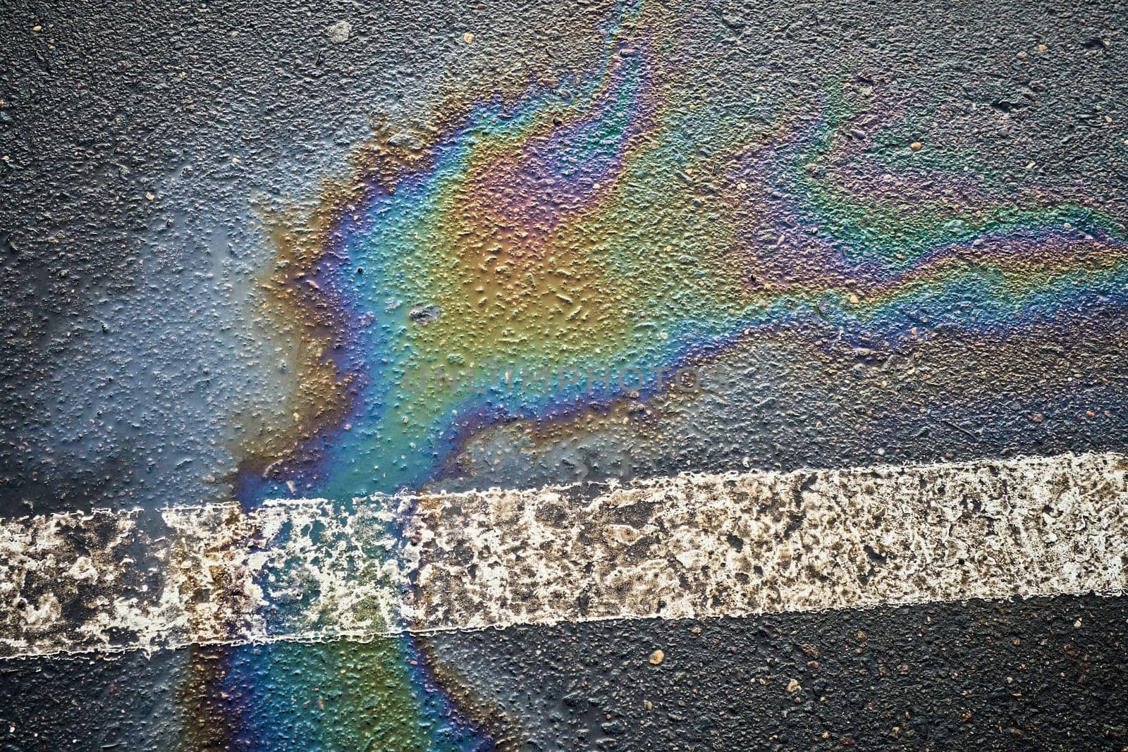 Colorful oil spill creating a striking pattern on asphalt near a parking lot.