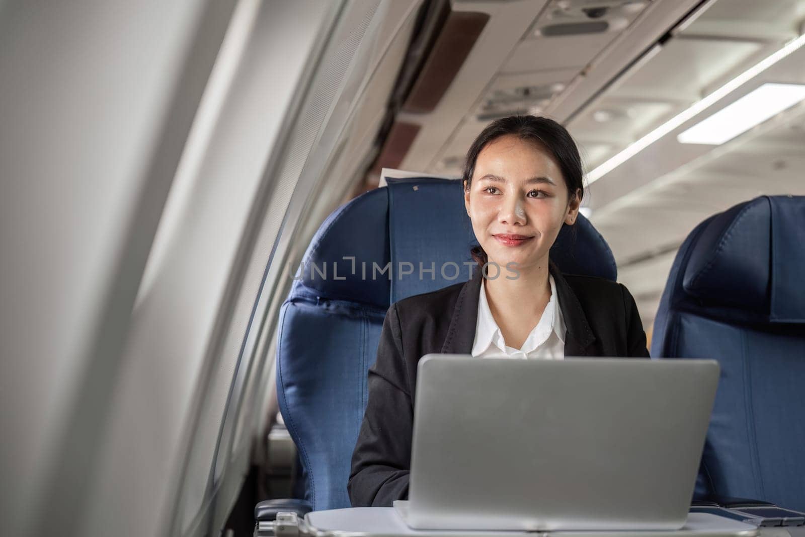 Businesswoman using a laptop on a plane, combining work and travel seamlessly.