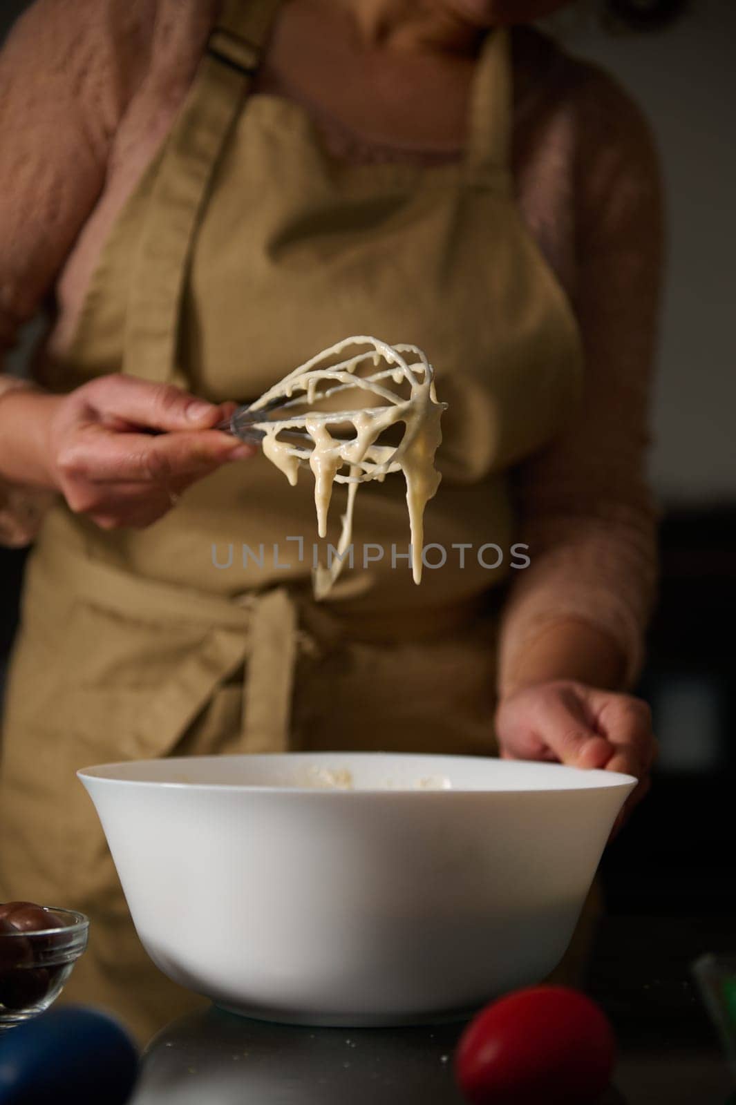 A person wearing an apron prepares liquid cake batter during a holiday baking activity. The whisk and bowl are central elements offering a cozy perspective on festive celebration preparations.