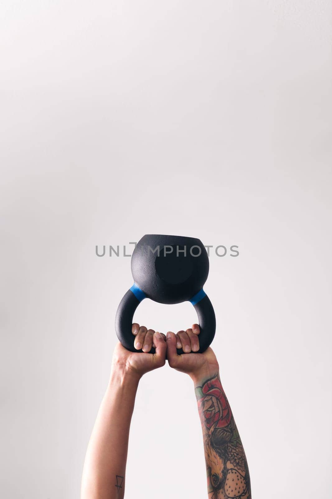 hands of strong woman with tattoos lifting heavy kettlebell white training in gym against white wall, , concept of fitness and active lifestyle, copyspace for text