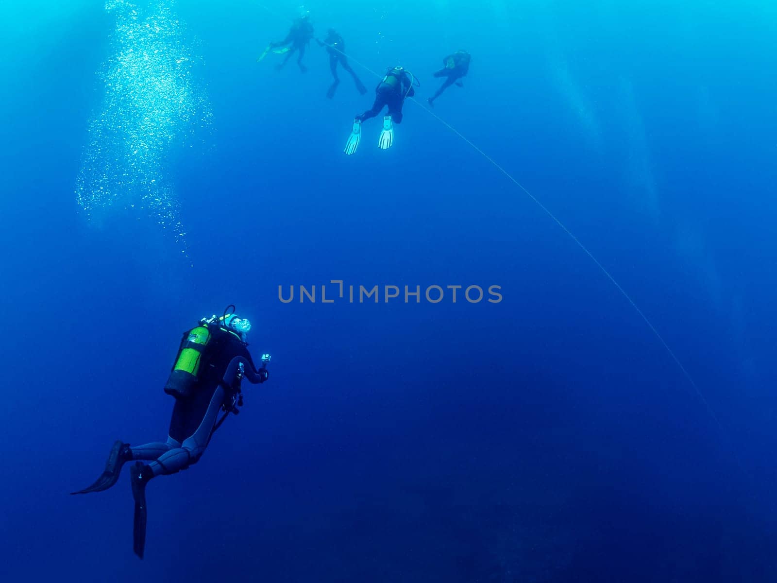 group of scuba divers in wetsuit diving holding on to the anchor line while making the safety stop before rising to the surface, concept of active leisure and underwater adventure, copyspace for text