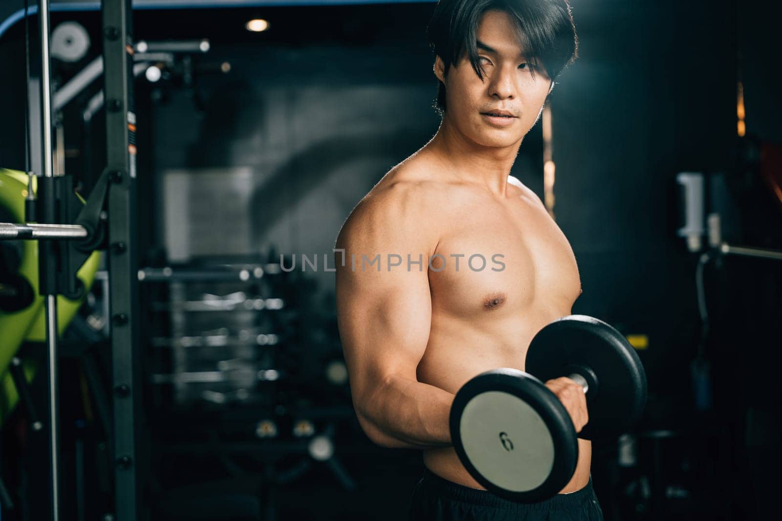 A muscular man with a strong physique lifts weights, his hand holding a heavy dumbbell, showing his hard work and dedication to his workout routine. Fitness GYM Healthy sports lifestyle concept