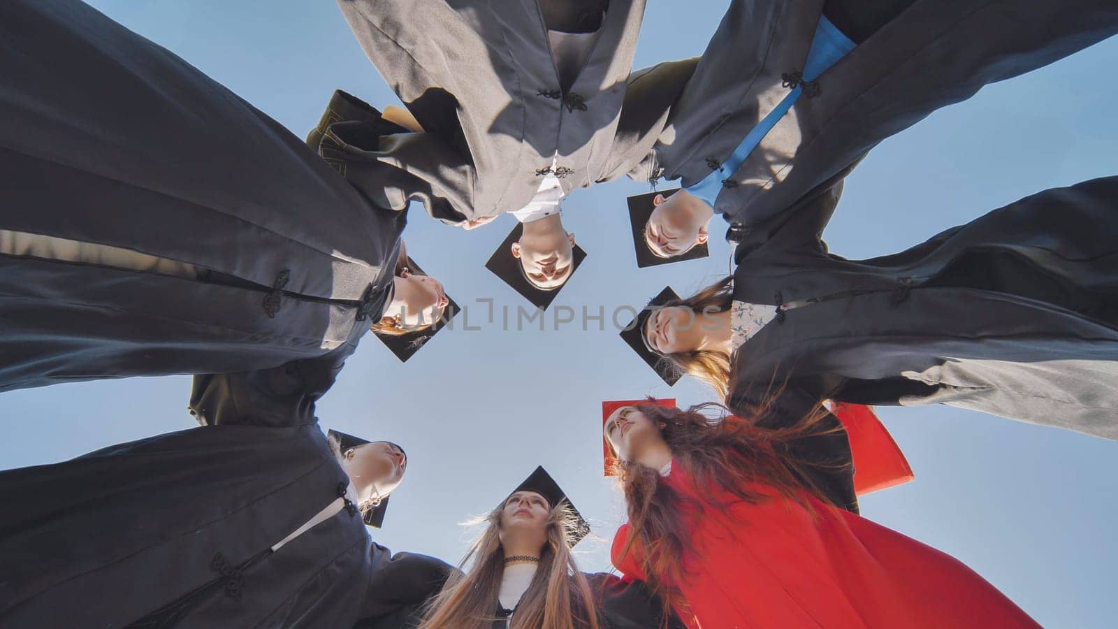 College graduates in a circle stand hugging each other