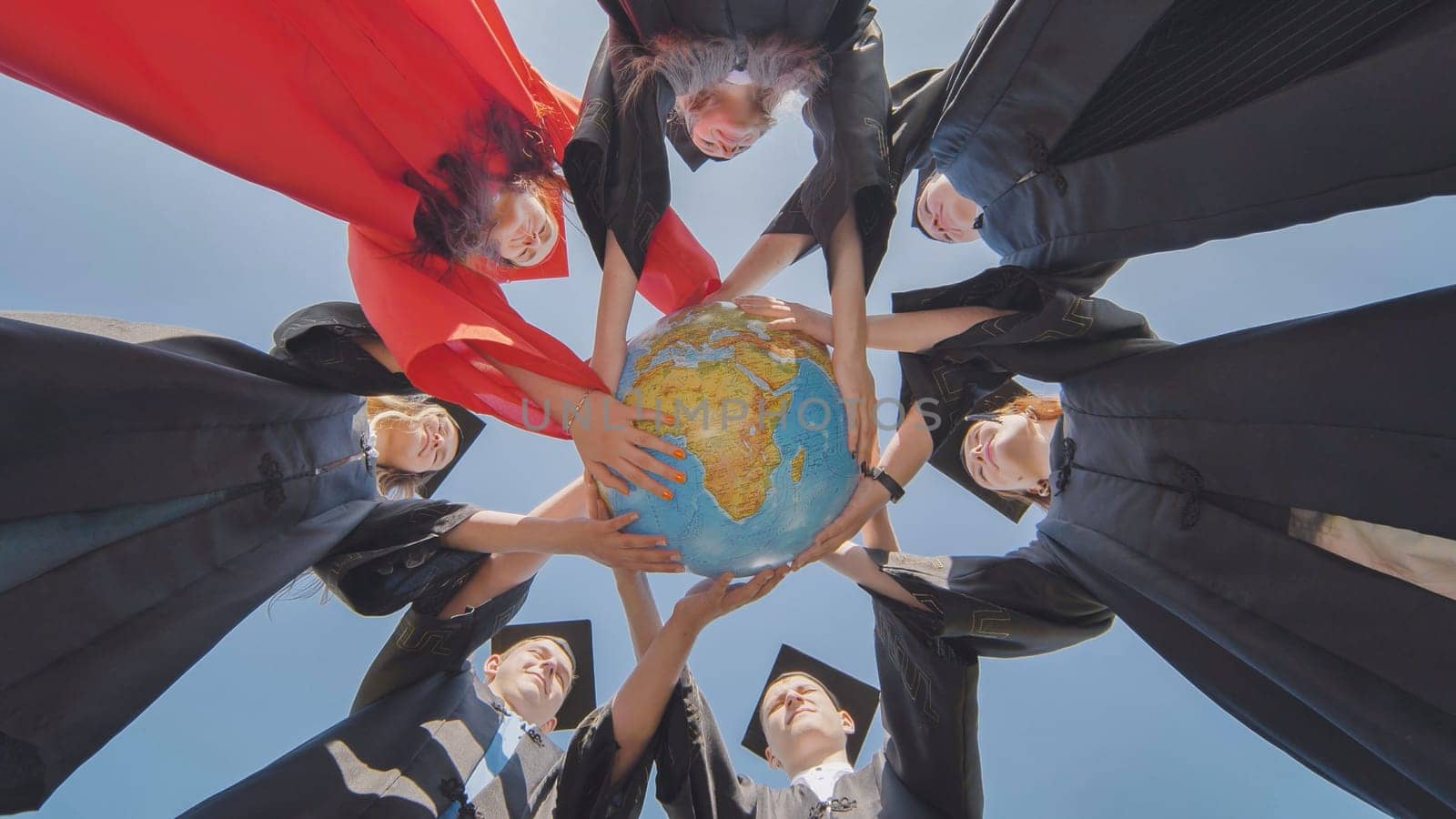 College graduates join hands over a globe of the world overlooking Africa. The concept of world peace