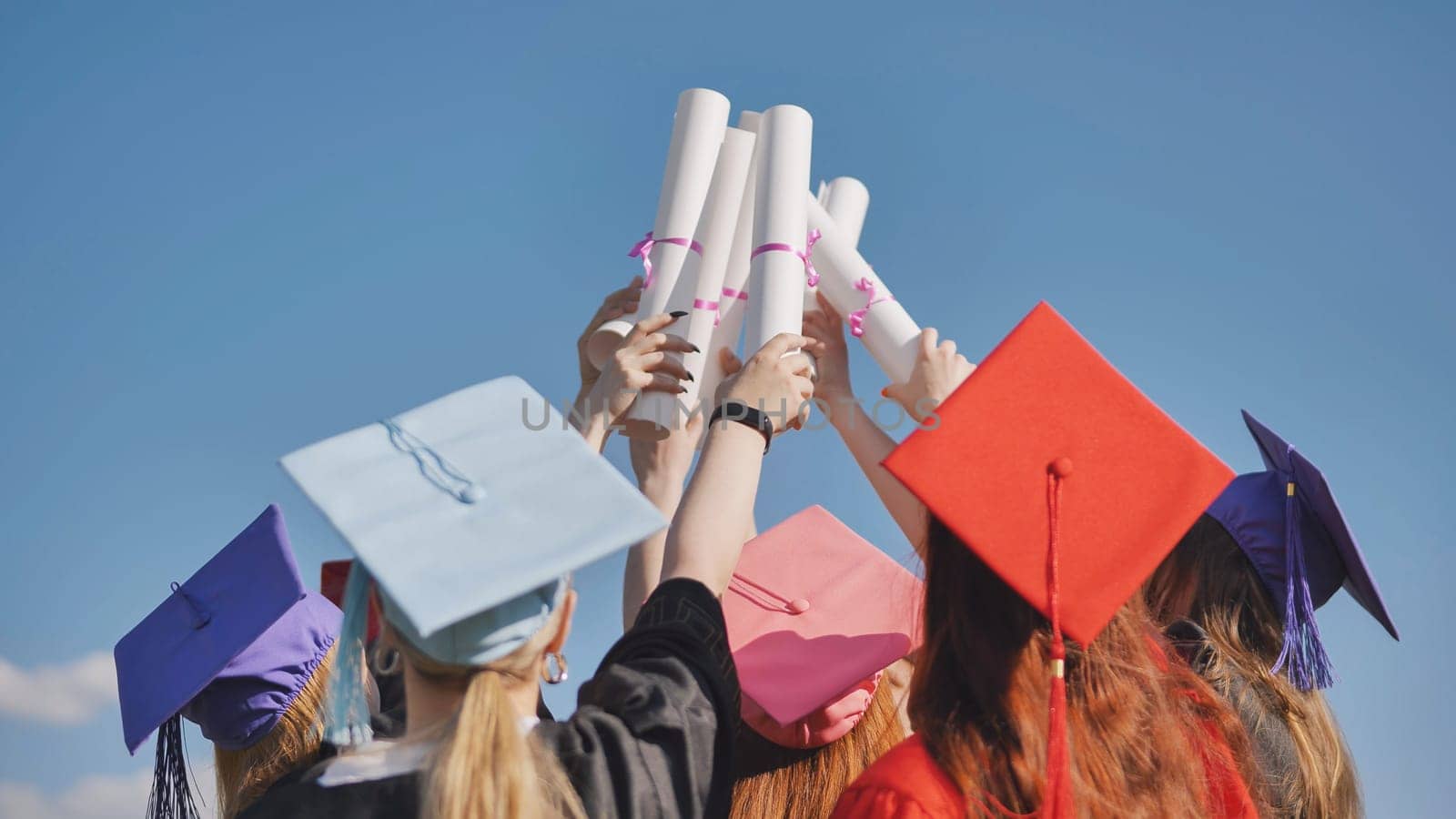 College graduates with multicolored caps tie their diplomas together