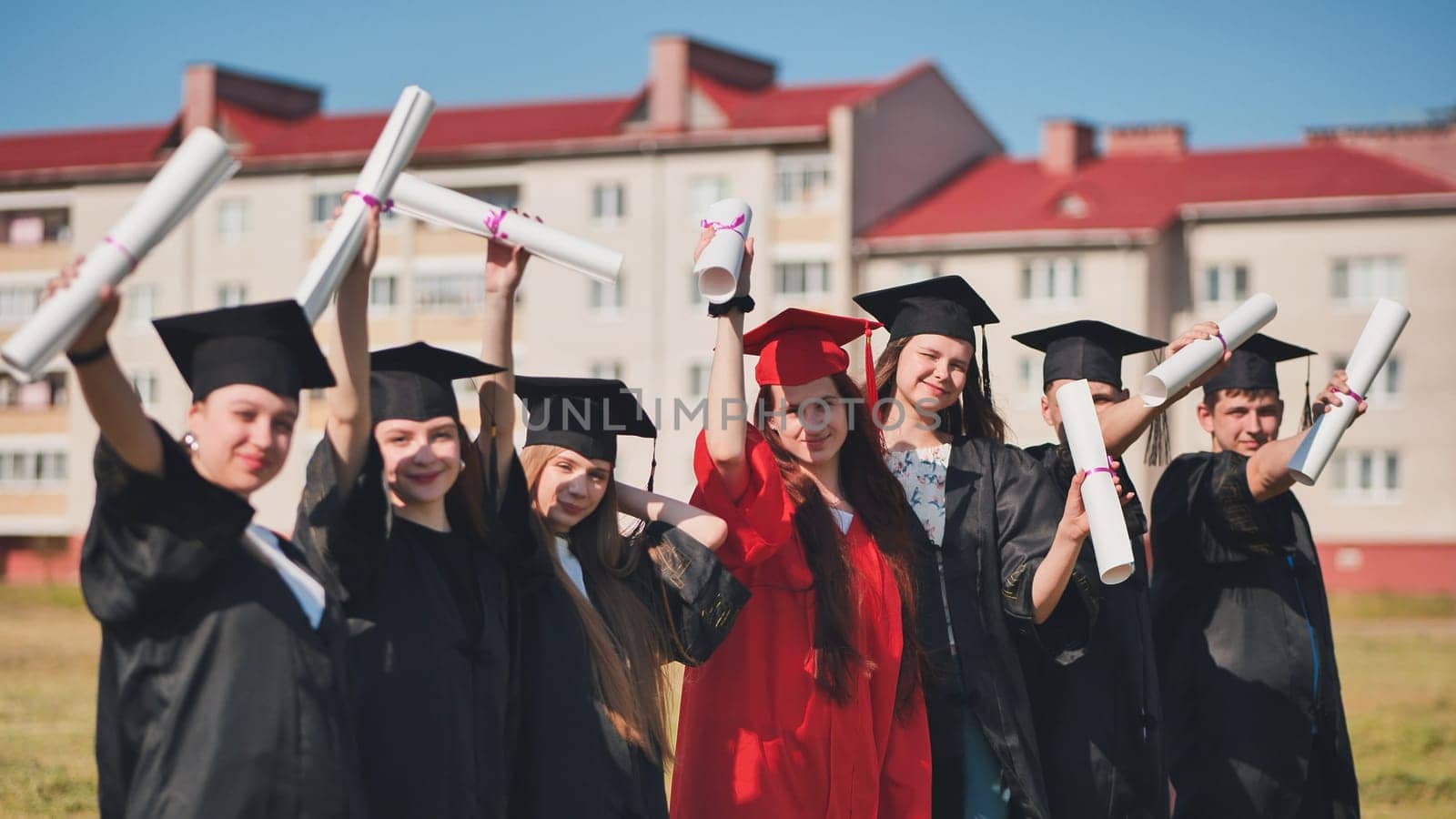 Young graduates pose and wave diplomas in their hands in the street. by DovidPro
