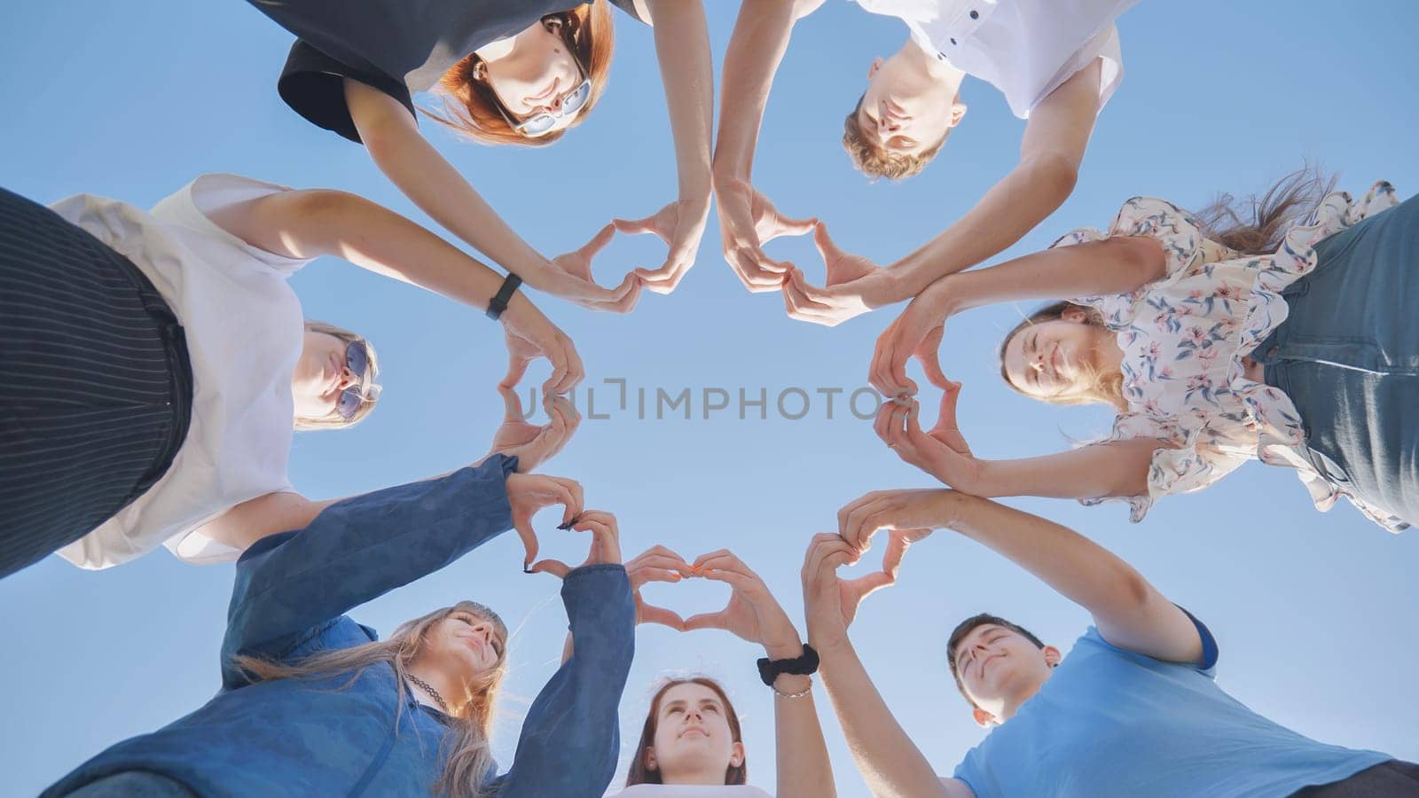 Group of seven people together doing an heart with their fingers and hands - people in cricle having fun and playing - ground view