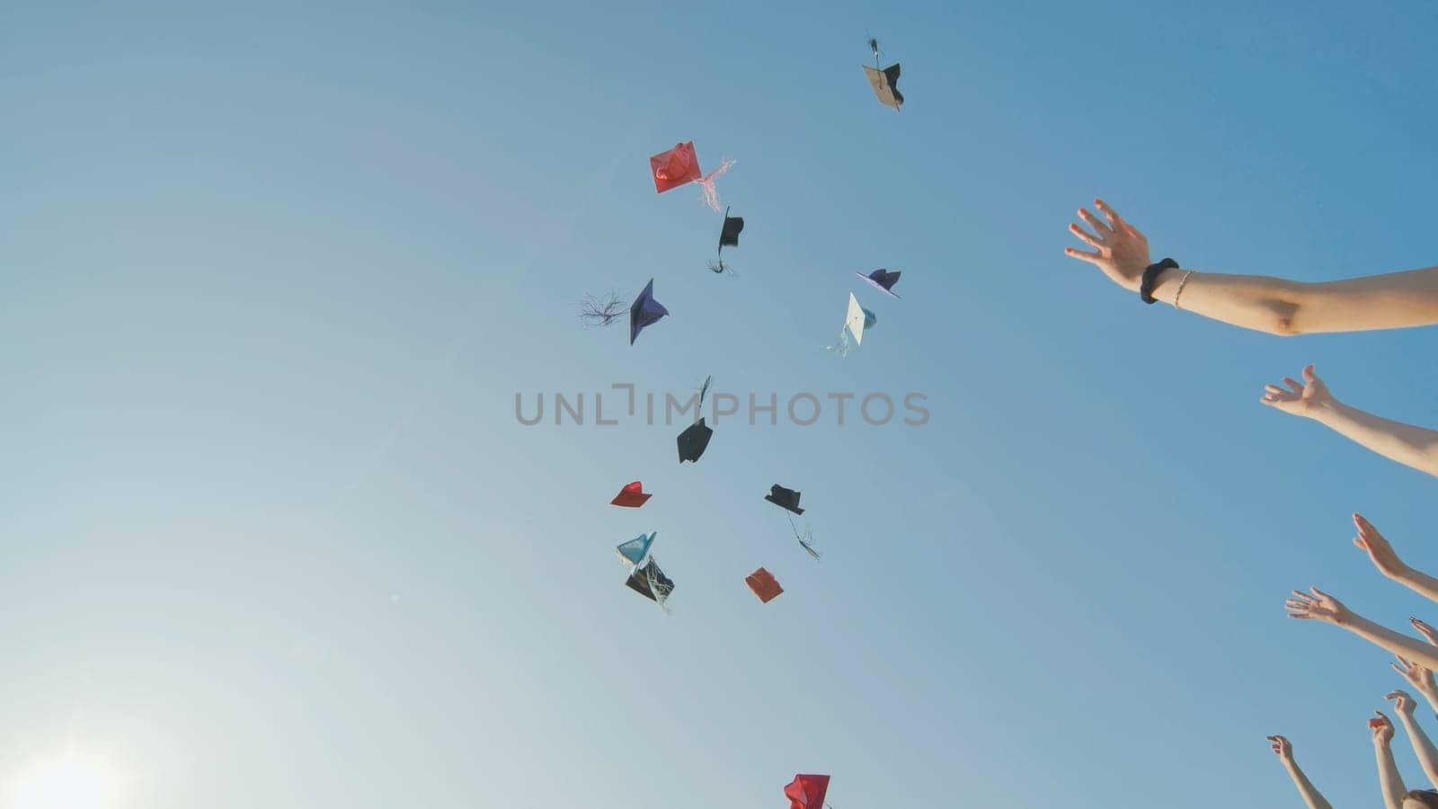 Graduates tossing multicolored hats against a blue sky