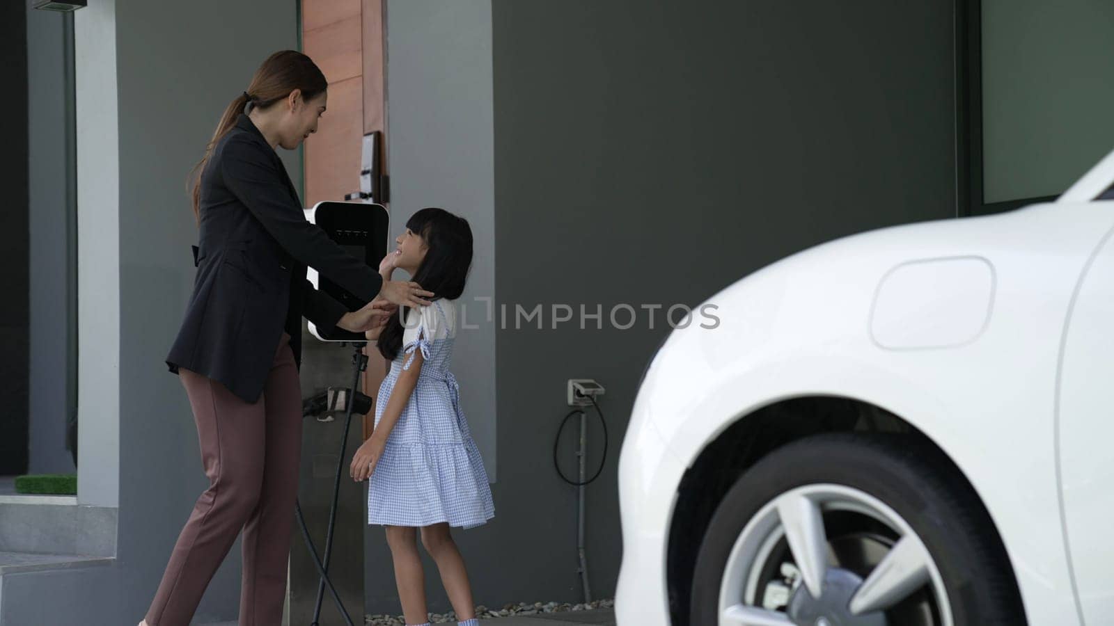 Progressive lifestyle of mother and daughter who have just returned from school in an electric vehicle that is being charged at home. Electric vehicle powered by sustainable clean energy.