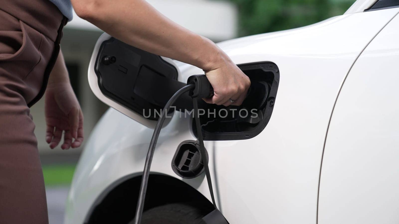 Progressive woman installing plug from home charging station to electric vehicle by biancoblue
