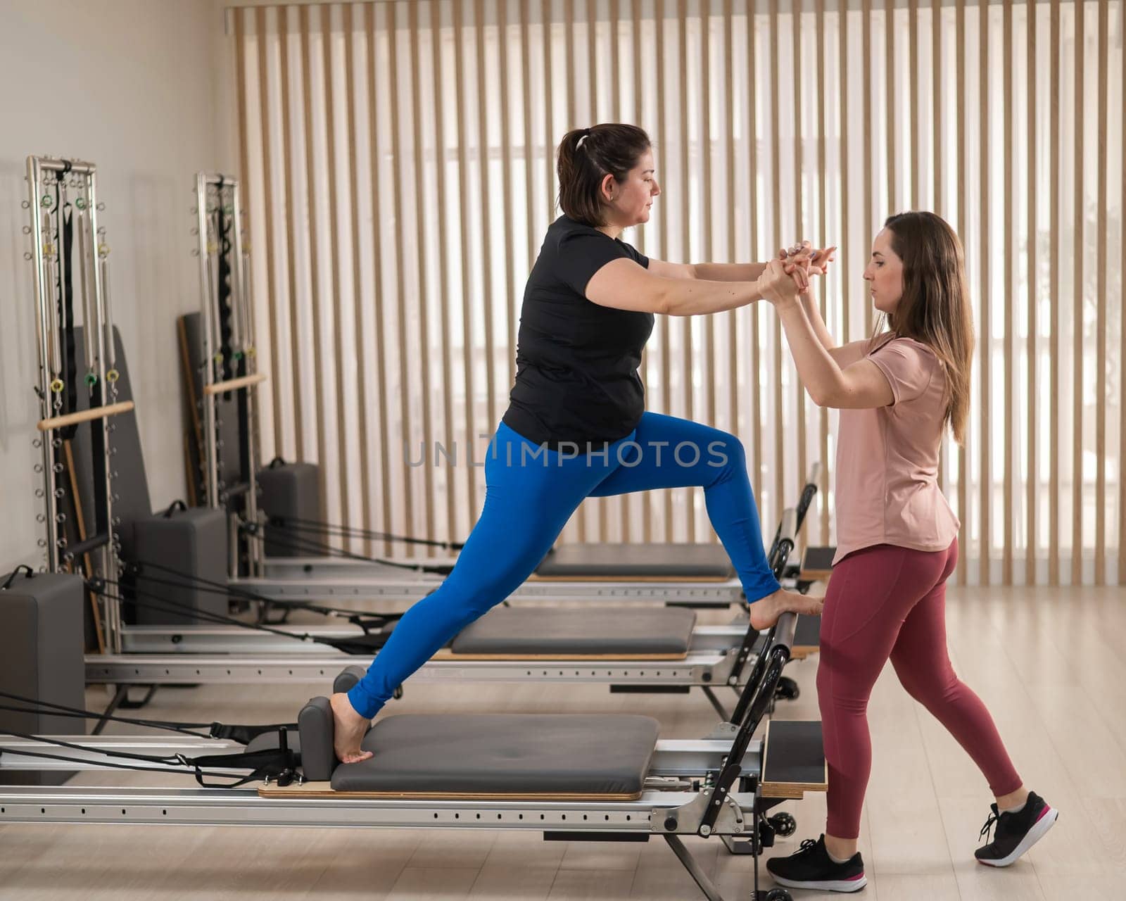 Overweight caucasian woman doing pilates exercises on reformer with personal trainer