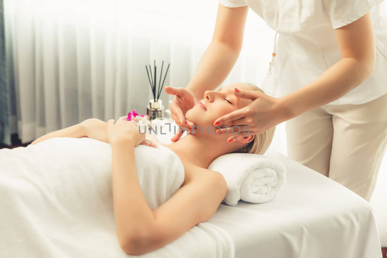 Caucasian woman enjoying relaxing anti-stress head massage and pampering facial beauty skin recreation leisure in dayspa modern light ambient at luxury resort or hotel spa salon. Quiescent