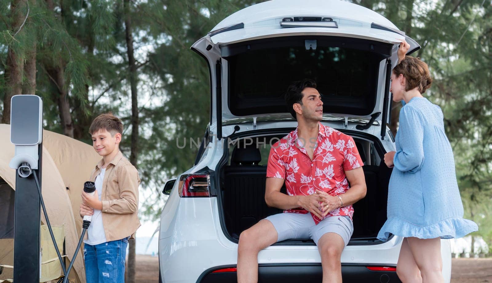 Outdoor adventure and family vacation camping in nature travel by eco friendly car for sustainable future. Lovely family recharge EV car with EV charging station in campsite. Perpetual