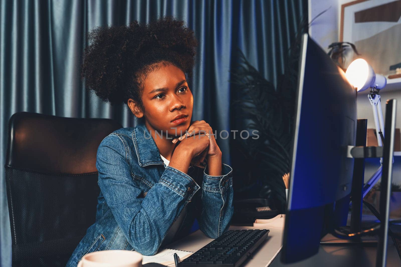 Young African creator looking on screen monitor laptop, wearing jeans shirt. Thinking the project or study new technology at workplace. Concept of job planing professional at home office. Tastemaker.