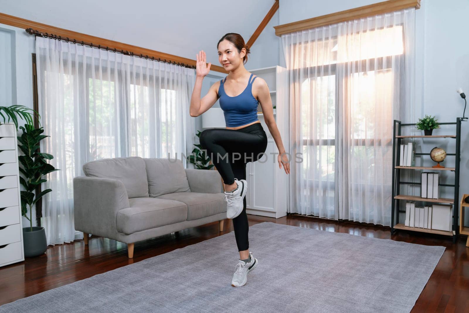 Energetic and strong athletic asian woman running in place at her home. Pursuit of fit physique and commitment to healthy lifestyle with home workout and training. Vigorous