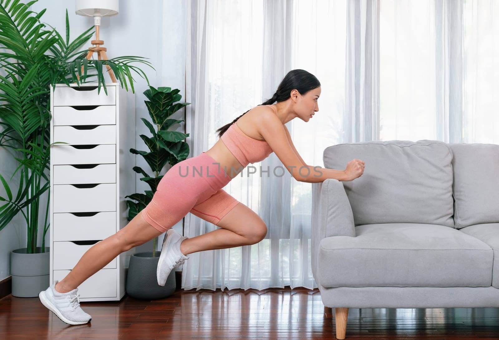 Fit young asian woman stretching her leg her body using sofa. Vigorous by biancoblue