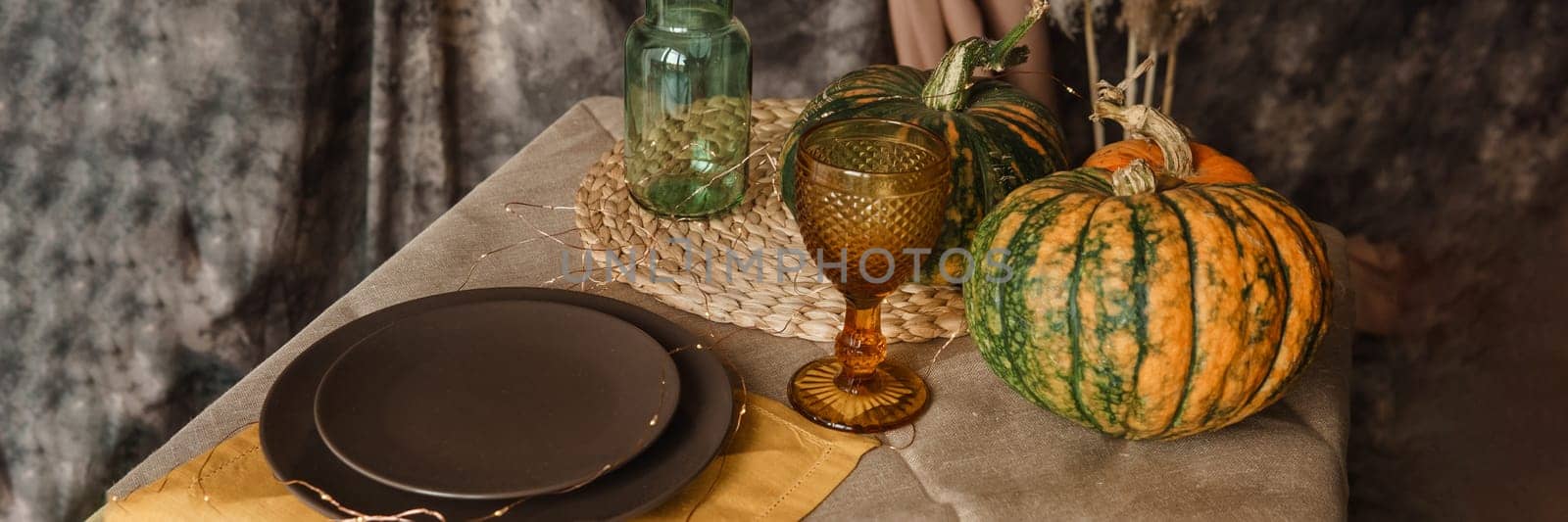 Autumn interior: a table covered with dishes, pumpkins, a relaxed composition of Japanese pampas grass. Interior in the photo Studio. Close - up of a decorated autumn table