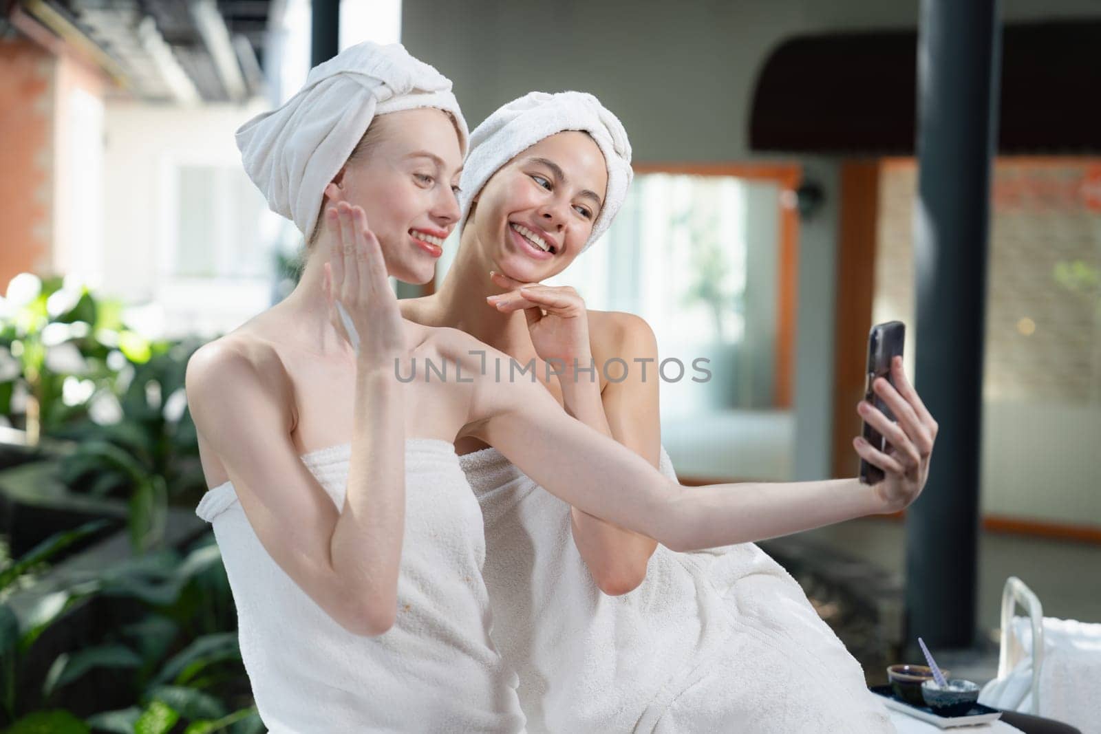 Couple of young beautiful women with beautiful skin in white towel taking a photo together at outdoor surrounded by peaceful natural environment. Beauty and healthy spa concept. Tranquility.