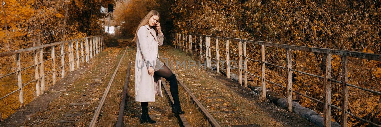 A beautiful long-haired woman walks through the autumn streets. Railway, autumn leaves, a woman in a light coat.