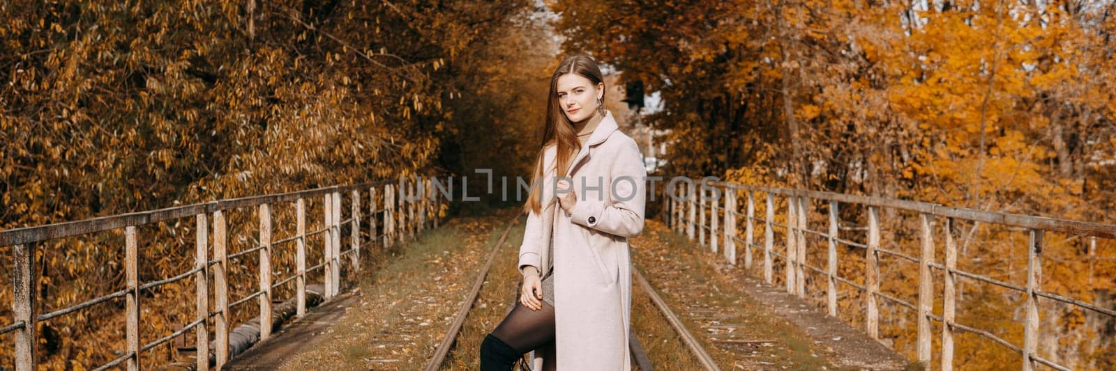 A beautiful long-haired woman walks through the autumn streets. Railway, autumn leaves, a woman in a light coat.