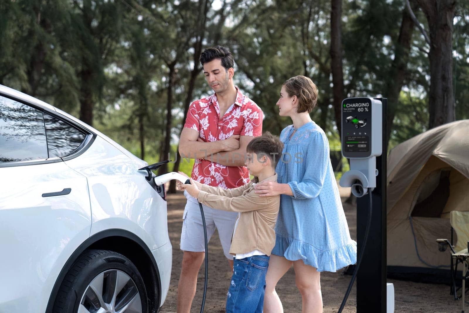 Outdoor adventure and family vacation camping in nature travel by eco friendly car for sustainable future. Lovely family recharge EV car with EV charging station in campsite. Perpetual