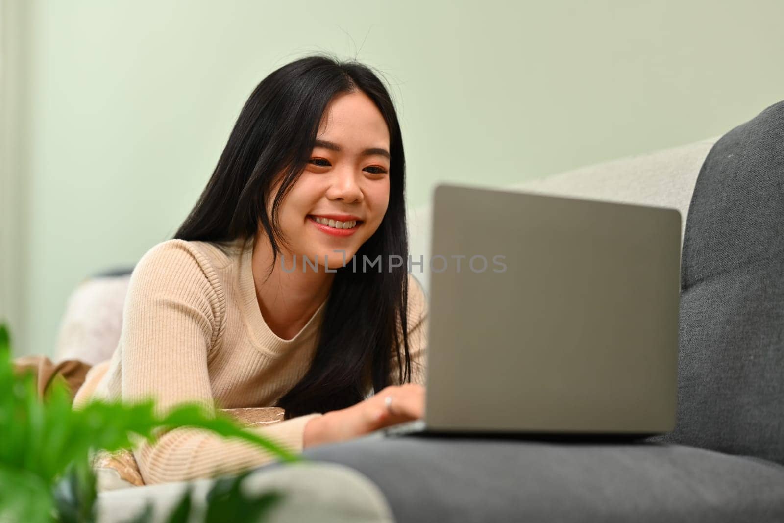 Carefree young woman lying on couch and using laptop. Technology, people and lifestyle concept.