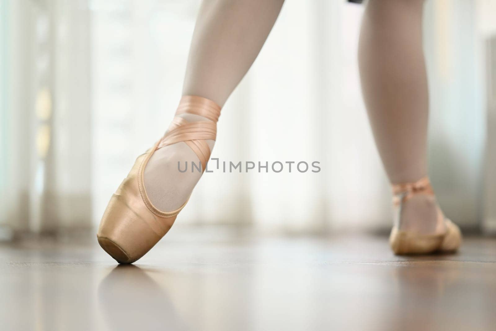 Ballerina feet in pink pointe shoes dancing on wooden floor. People, dance art, education and flexibility concept.