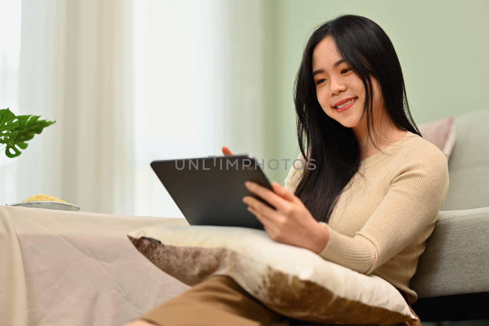 Cute, smiling young woman using digital tablet in living room. Technology, people and lifestyle concept.