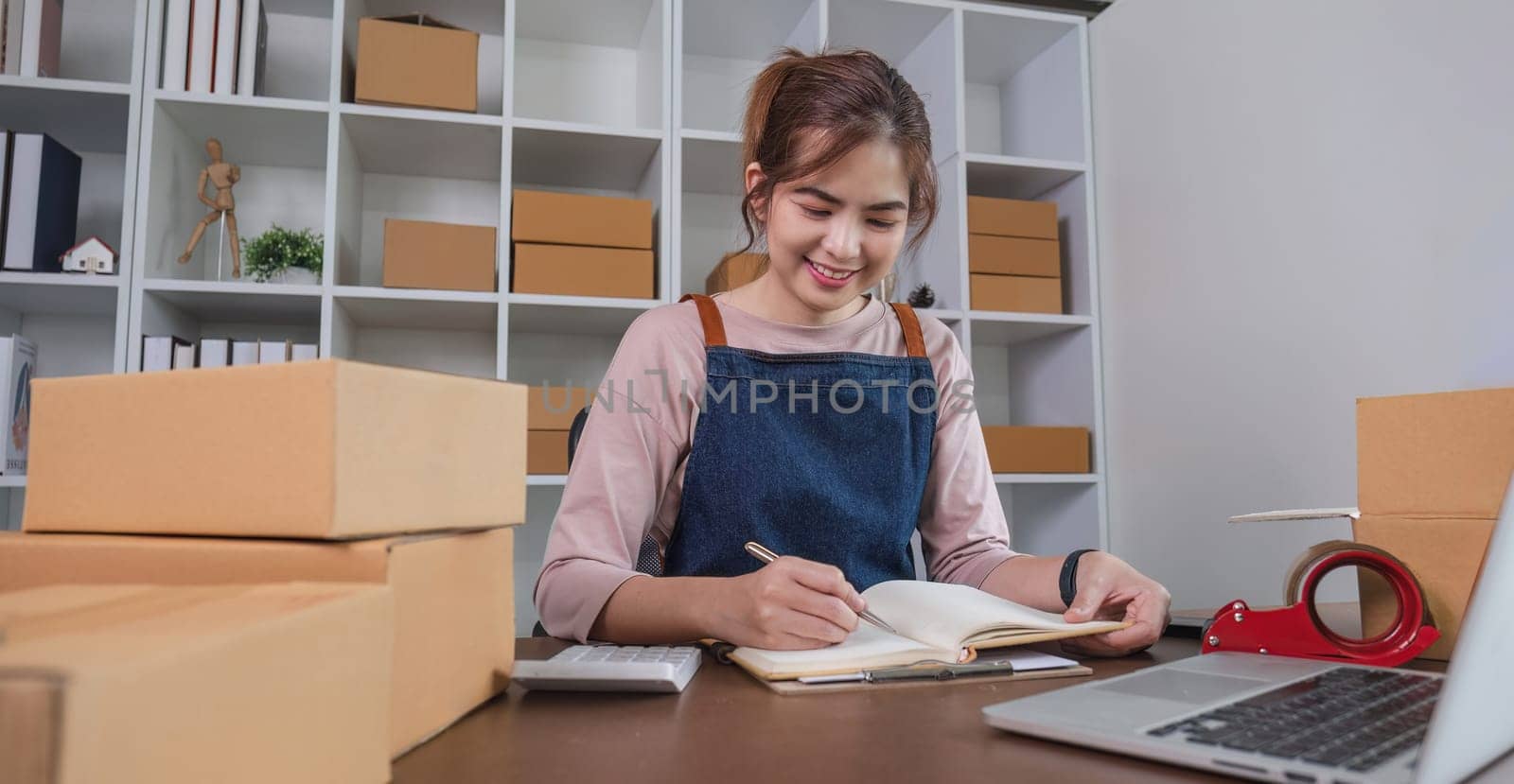 Entrepreneur using calculator with pencil in her hand, calculating financial expense at home office,online market packing box delivery,Startup successful small business owner, SME, concept by wichayada