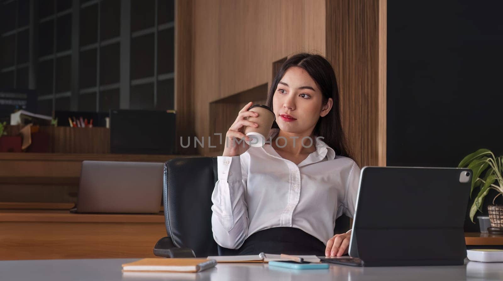 Asian businesswoman drinking coffee with tablet on desk at office. by wichayada