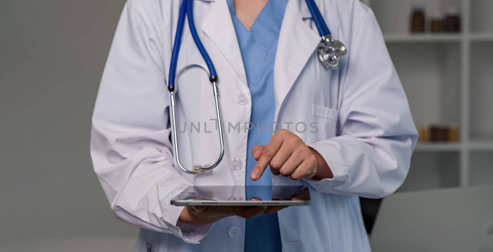 Portrait of a smiling female doctor holding a digital tablet wearing a medical coat and stethoscope in hospital by wichayada