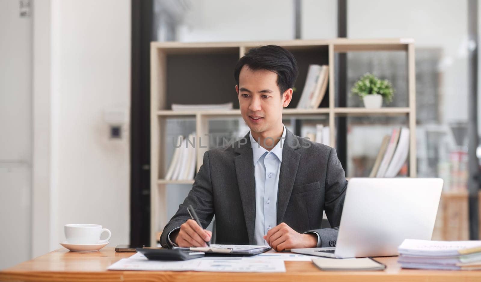 Focused businessman working with laptop documents in office holding papers preparing report analyzing work results, analyst doing paperwork at workplace using computer.