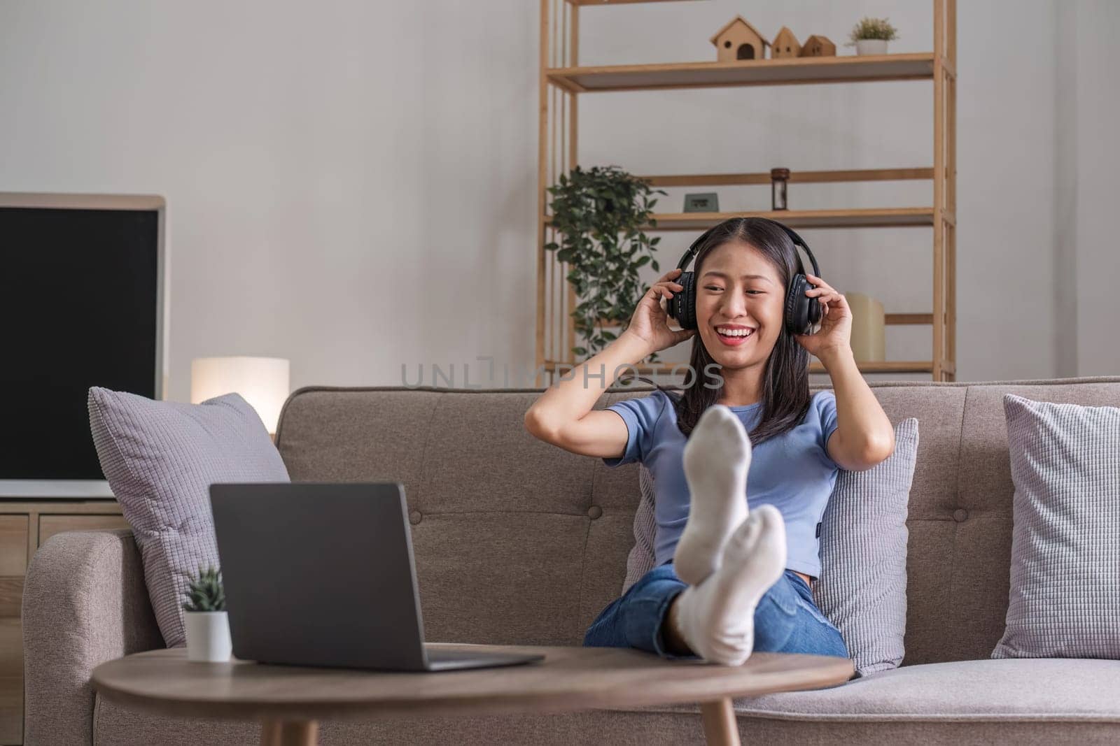 Woman listening music in headphones while lying on sofa in room by wichayada