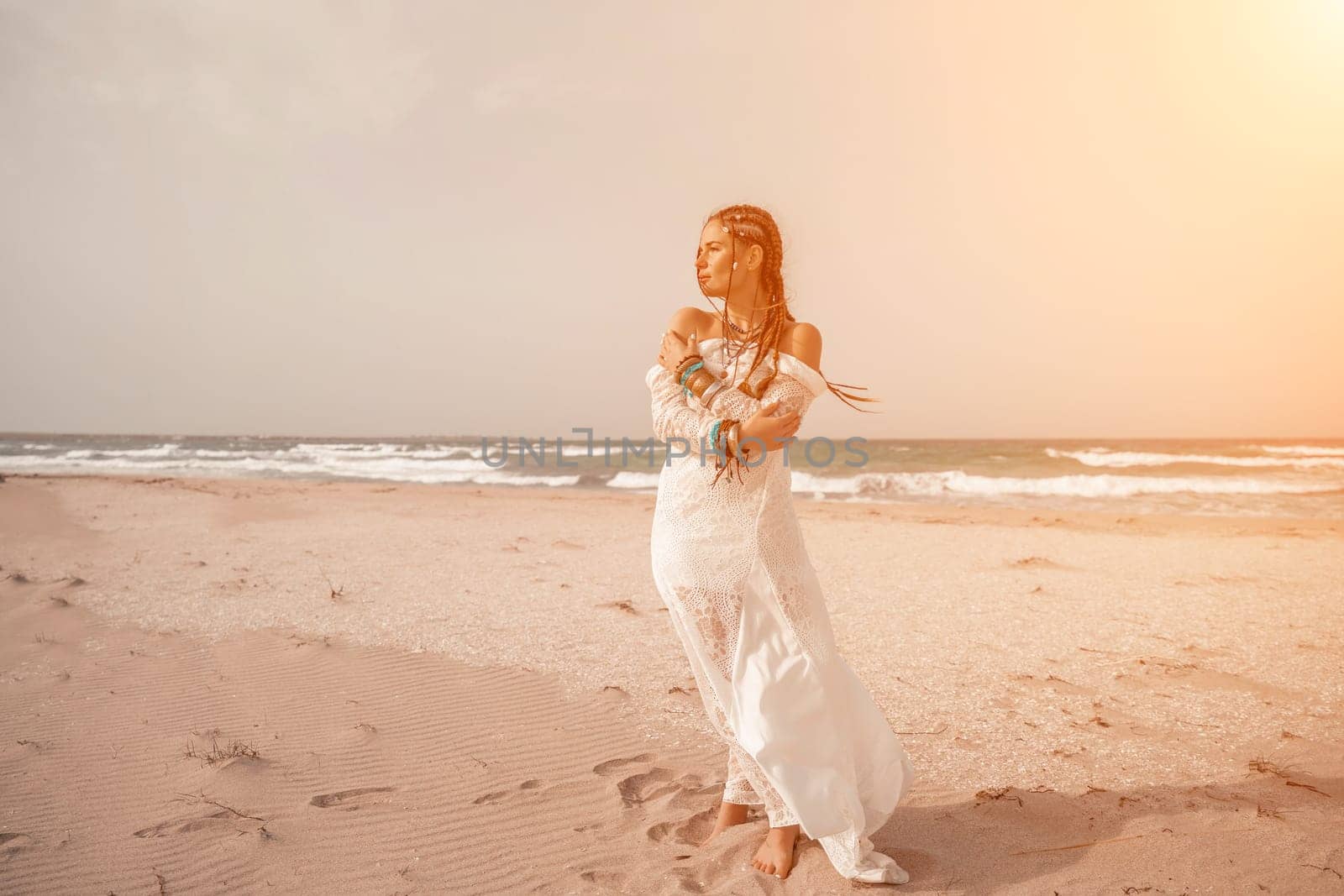 woman sea white dress. Model in boho style in a white long dress and silver jewelry on the beach. Her hair is braided, and there are many bracelets on her arms. by Matiunina