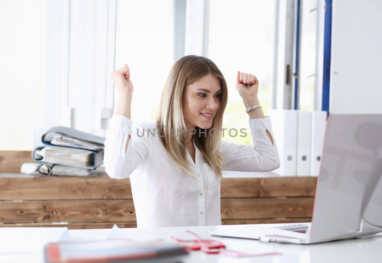 Beautiful joyful woman at workplace using computer pc celebrate something with arms up. Big deal salary promotion lottery win discount vacations approval sale result feel fun good news concept