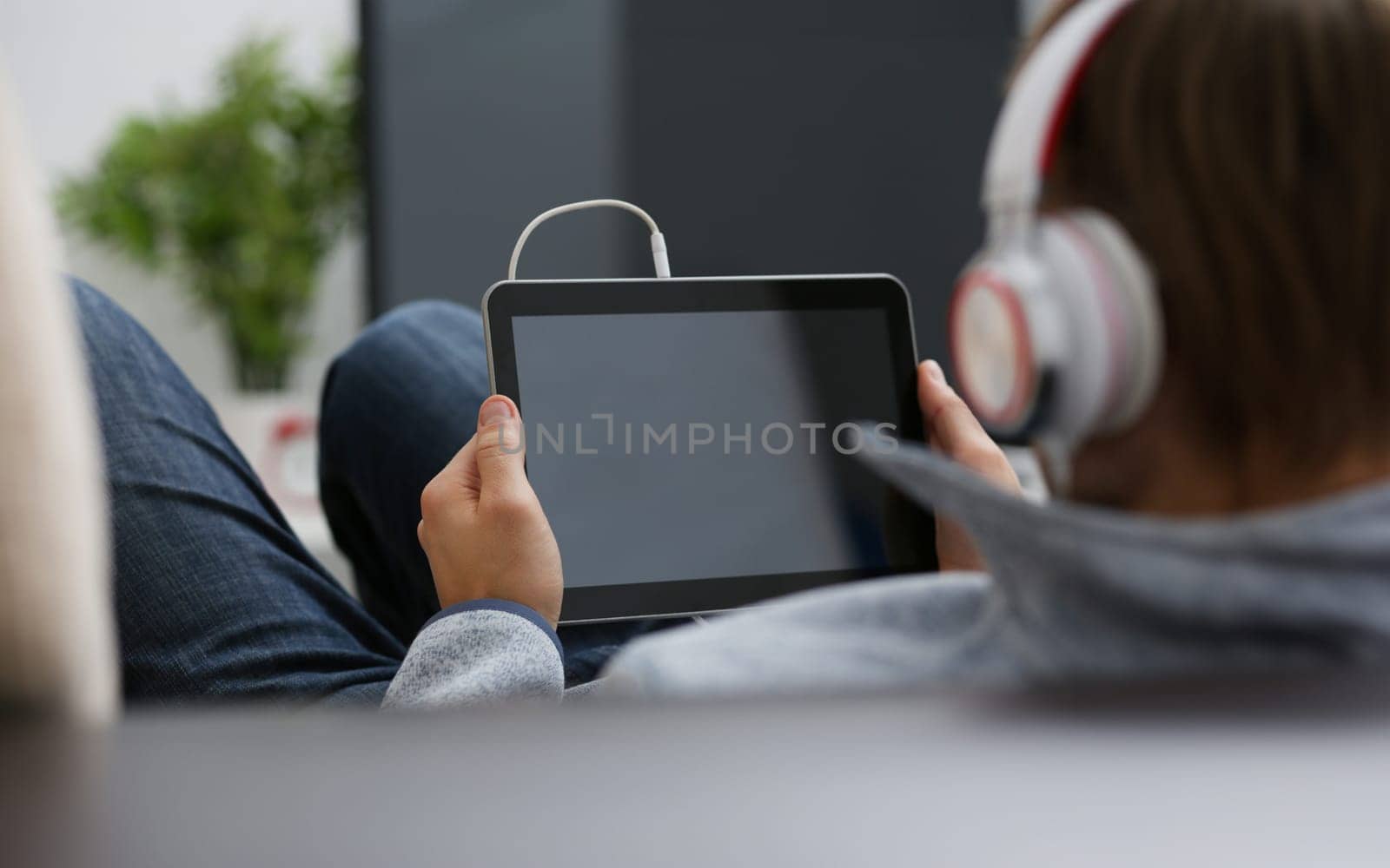 Male hand holds tablet pad in home setting while sitting on the couch engaged an internet surfing. Using application to press a finger on the display leisure listering music concept closeup.