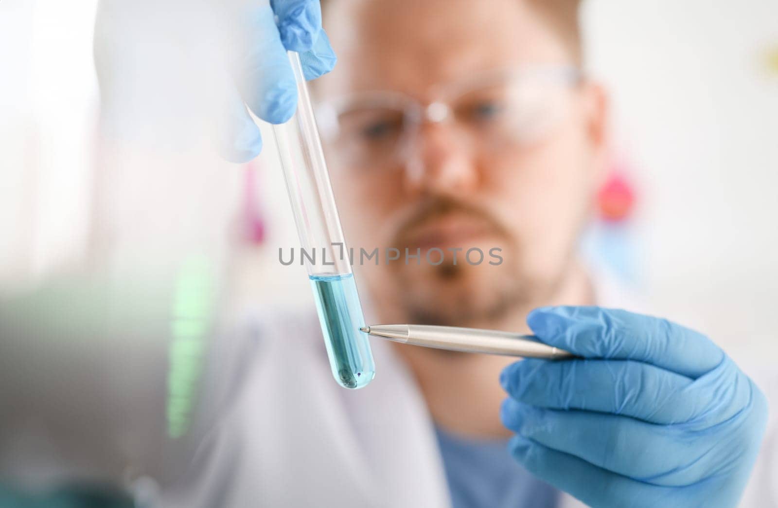 A male chemist holds test tube of glass in his hand overflows a liquid solution of potassium permanganate conducts. Analysis reaction takes various versions of reagents using chemical manufacturing.