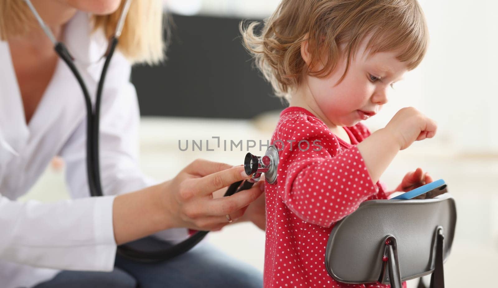 Little child with smarthone at doctor reception. Physical exam cute infant portrait baby aid healthy lifestyle ward round child sickness specialist clinic test pulse concept addiction