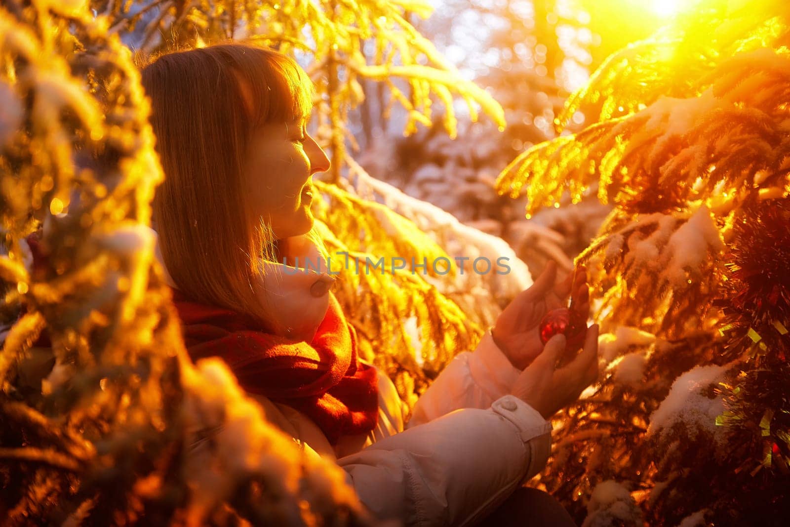 A middle-aged woman strolls through a snowy forest, admiring the beauty of winter while holding a festive ornament in her hands.