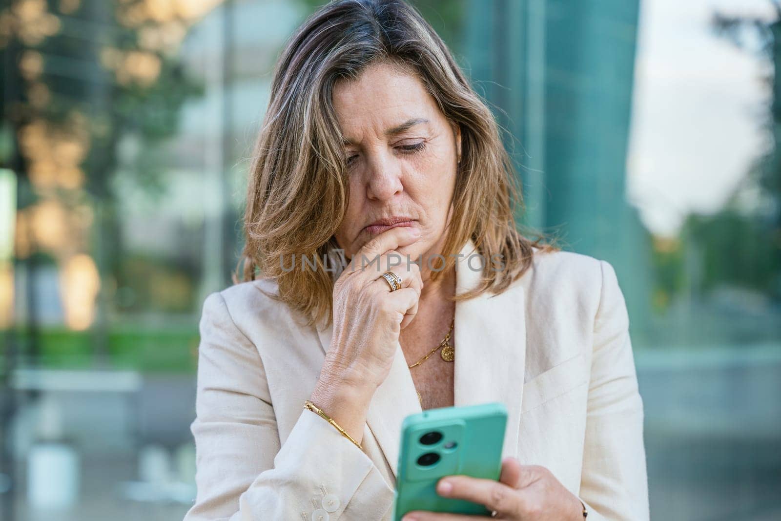 Smiling middle-aged businesswoman using a smartphone outdoors in a modern urban setting.