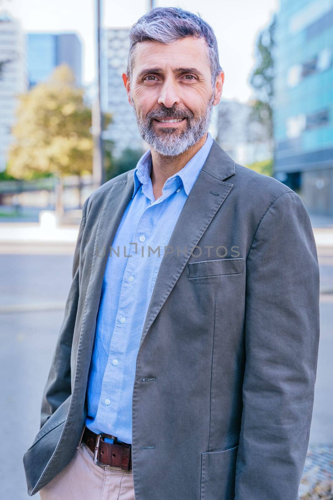 Portrait of a smiling middle-aged businessman in a smart casual outfit standing outdoors in a modern urban environment, exuding confidence and professionalism.