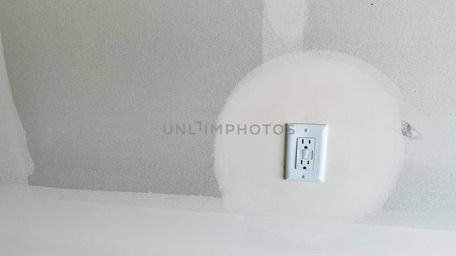 Castle Pines, Colorado USA - January 18, 2023-A GFCI outlet installed on a partially finished garage wall in a new single-family home under construction. The drywall shows a sanded area around the outlet, indicating ongoing preparation for painting or finishing.