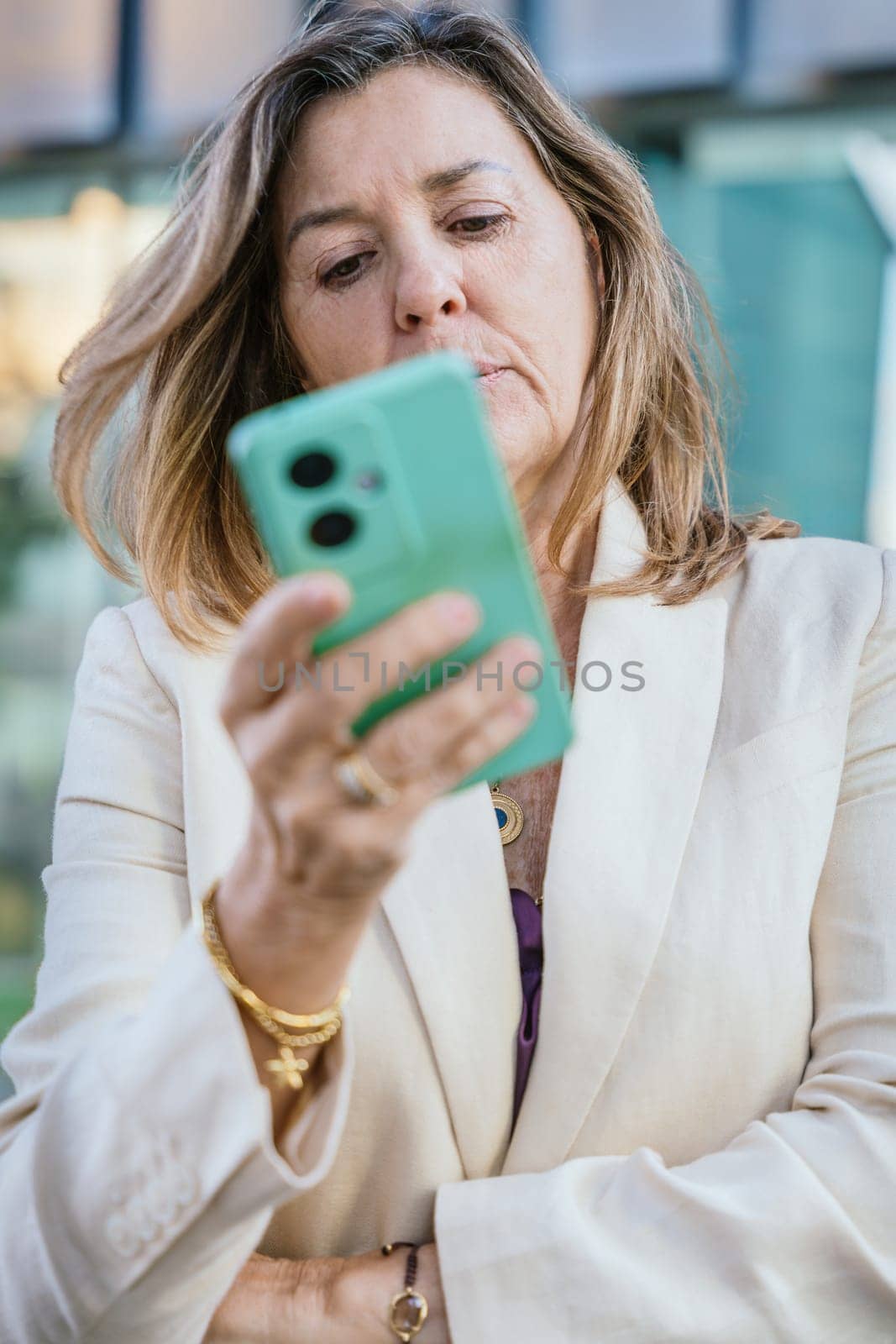 Smiling middle-aged businesswoman using a smartphone outdoors in a modern urban setting.