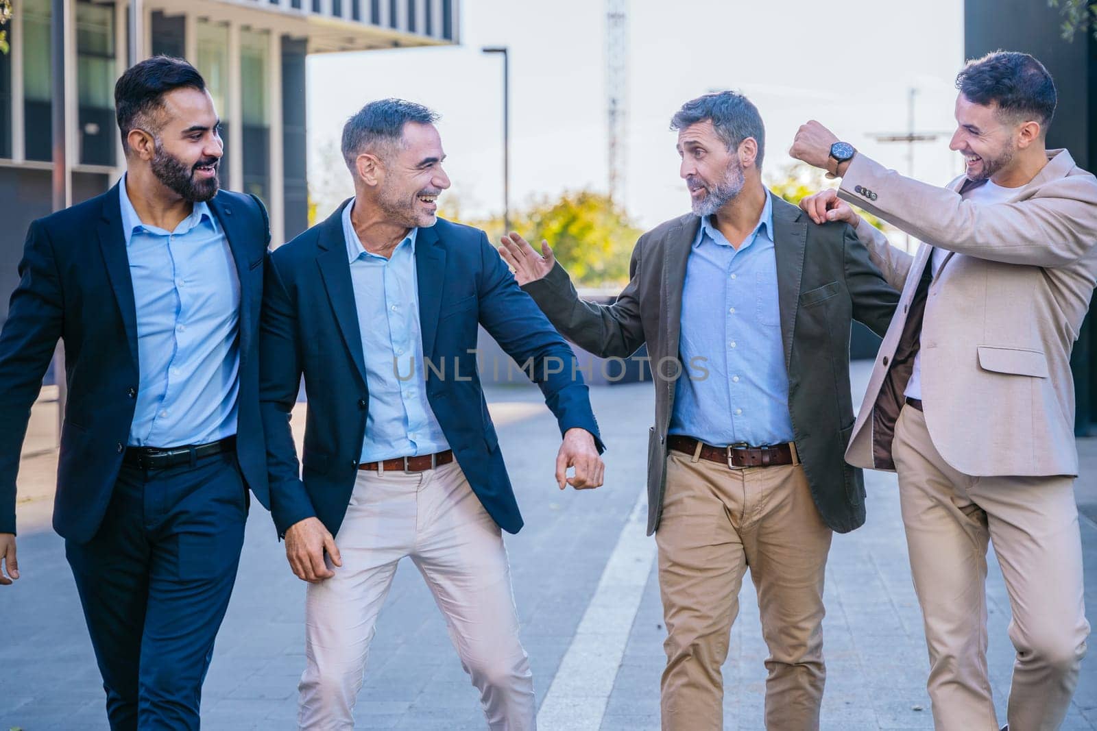 Four businessmen in smart casual and formal attire outdoors in an urban setting, laughing and celebrating success, demonstrating teamwork and positive energy.